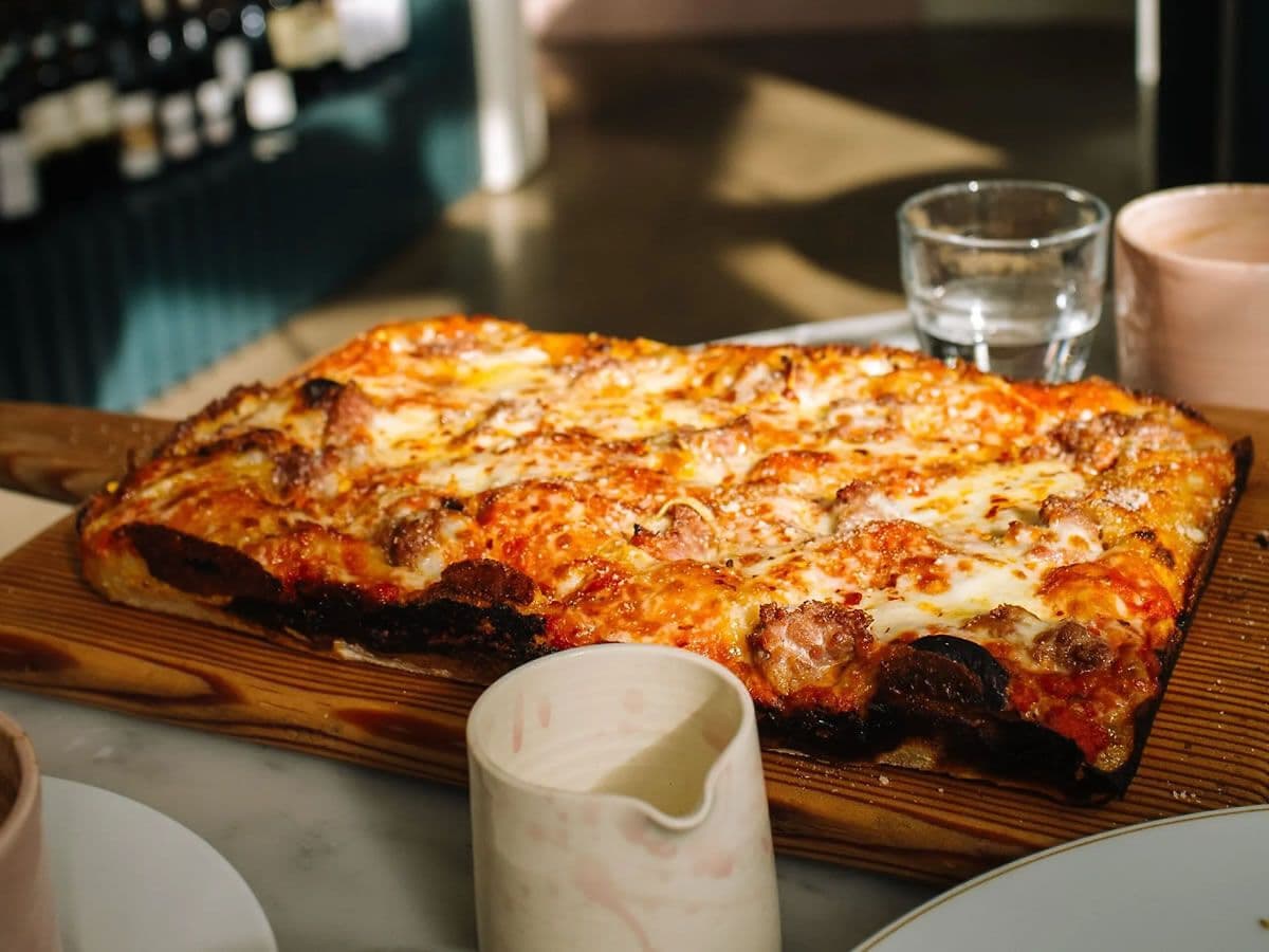 Une pizza alla romana en plaque, croûte dorée et tachetée de brun, sur une planche en bois